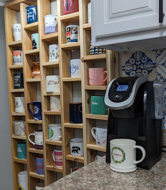 Collection of festive mugs displayed on wooden shelves, with a coffee maker nearby, capturing wholesome Christmas vibes.