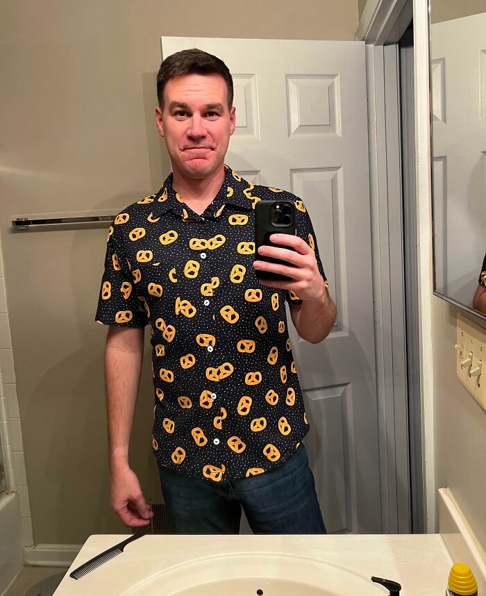 Man in pretzel-patterned shirt taking a mirror selfie, smiling widely. Wholesome-Christmas-Posts.