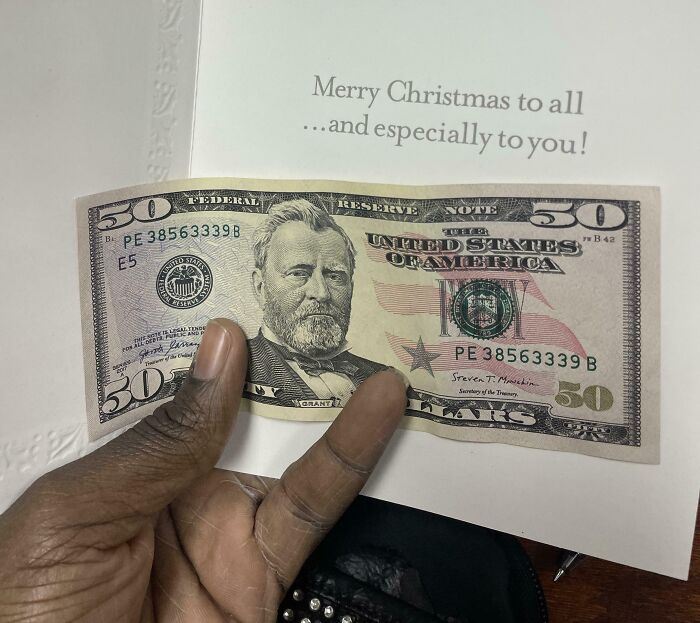 A hand holding a $50 bill inside a card reading "Merry Christmas to all and especially to you."