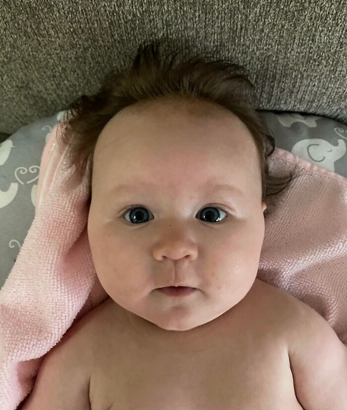 Baby wrapped in a pink towel, embodying a wholesome Christmas vibe with big eyes and playful hair.