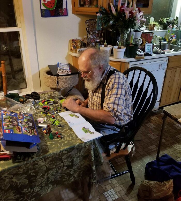 A man assembling LEGO at a kitchen table, surrounded by Christmas-themed items, evoking a wholesome holiday spirit.