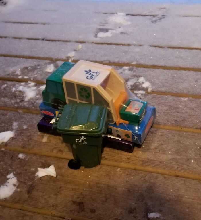 Toy recycling truck and bin on a snowy wooden deck.