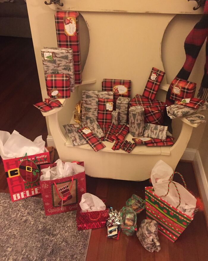 Christmas presents wrapped in festive paper and bags, neatly arranged on a white chair and wooden floor.