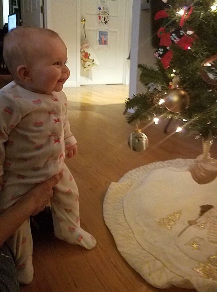 Baby in pajamas smiling at a decorated Christmas tree, capturing a wholesome Christmas moment.