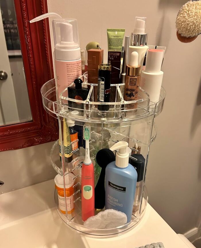 Acrylic organizer on a bathroom counter with skincare and hygiene products neatly arranged.