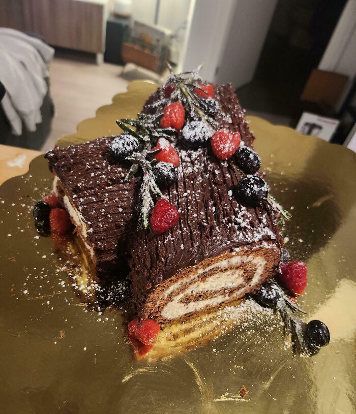 Chocolate Yule log topped with berries and powdered sugar, a festive Christmas snack food idea on a gold platter.