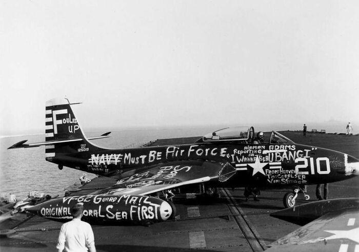 Historical photo of a World War II fighter plane on a carrier deck, with graffiti celebrating the end of war.