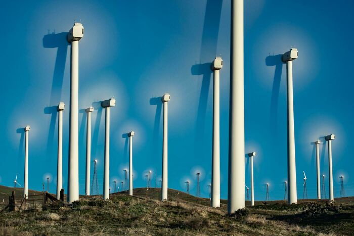 Wind turbines on grassy hills under a blue sky, resembling computer-generated renders.