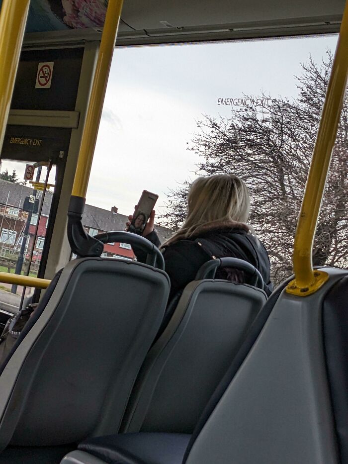 Person on a bus, taking a selfie with phone, embodies lazy-infuriating-people behavior.