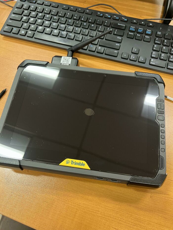 A dirty tablet screen showing a fingerprint mark, with a keyboard on a wooden desk, illustrating lazy habits.