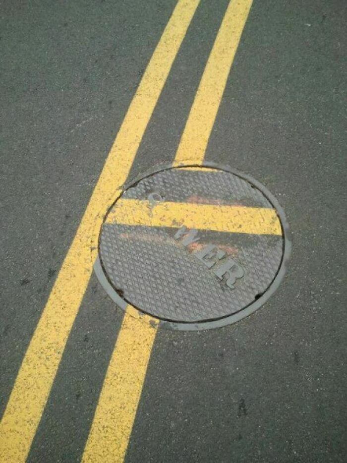 Manhole cover misaligned with painted yellow road lines, symbolizing laziness.