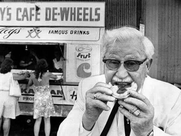 Elderly man eating a sandwich in front of a vintage food truck, showcasing historical moments.