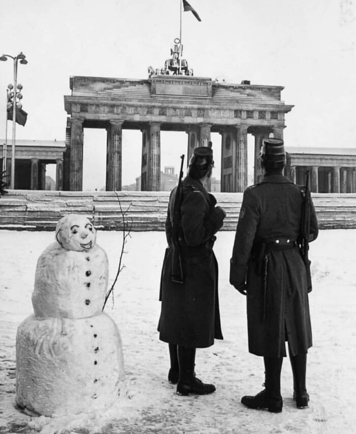 Historical picture of two soldiers by a snowman, facing the Brandenburg Gate in winter.