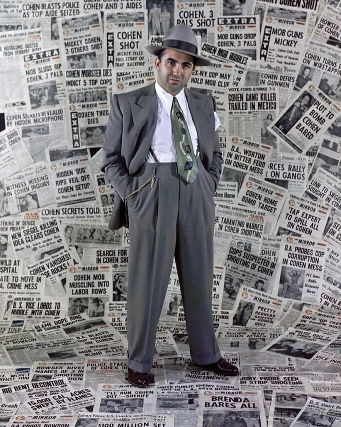 Man in vintage suit stands in a room covered with historical newspaper headlines, evoking past influence on the future.