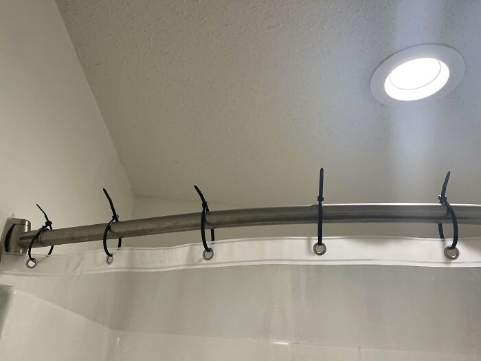 Shower curtain hung with zip ties on a rod, a creative example of lazy-infuriating-people solutions.