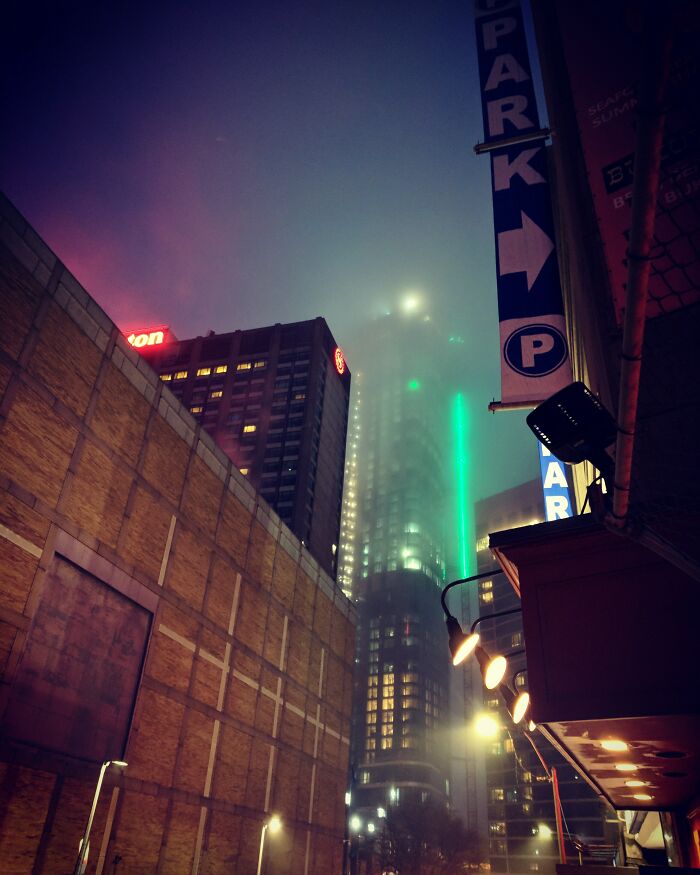 Foggy cityscape at night, illuminated by neon lights, resembling a videogame environment.