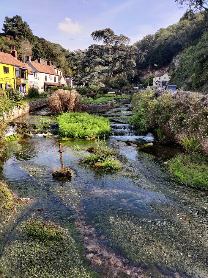 A picturesque village scene with a stream resembling a videogame, featuring houses and lush greenery.