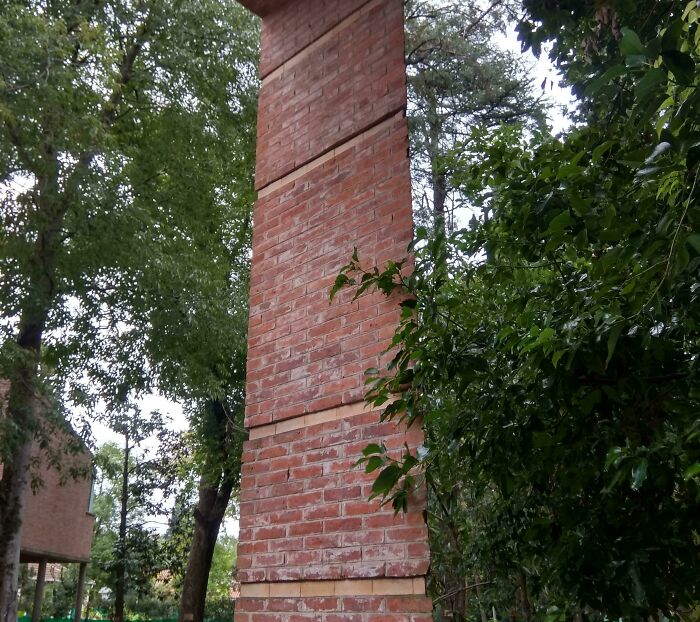 Brick column in a forest setting, resembling a bad render with sharp, unrealistic edges.