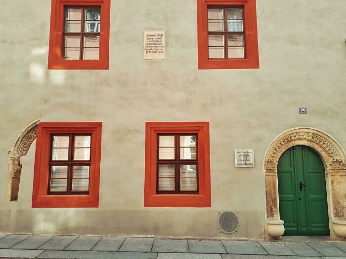 Building facade with vivid orange window frames and green door, resembling bad renders.