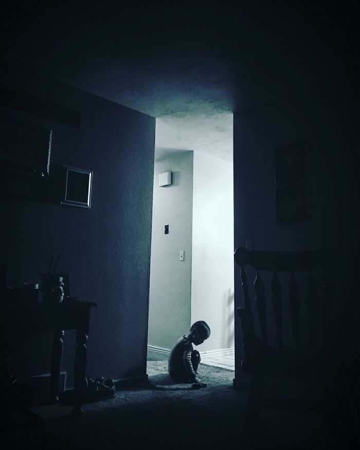 A child sitting in a dimly lit hallway, resembling a scene from a videogame.