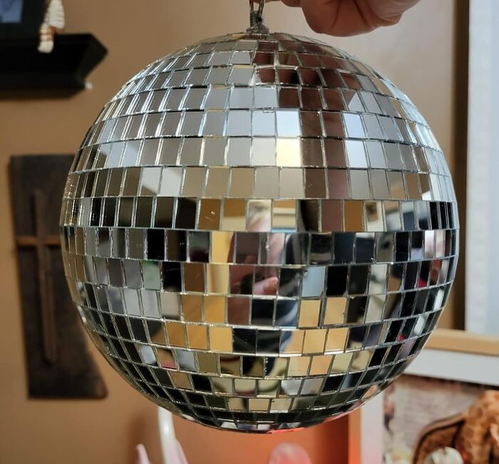 A hand holding a shiny disco ball, reflecting a room, illustrating Nye hosting tips.