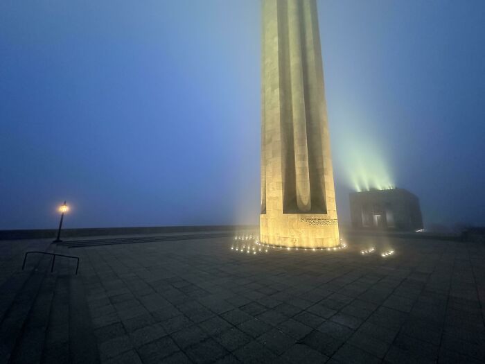 Tall illuminated tower in fog, resembling a scene from a video game.