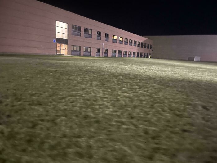 A night view of a building with glowing windows on an empty grassy field, resembling a scene from a game.