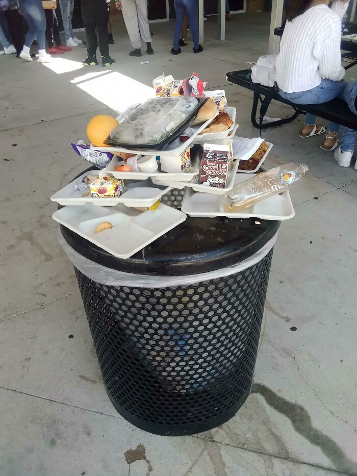 Overflowing trash can with food trays, illustrating lazy behavior.