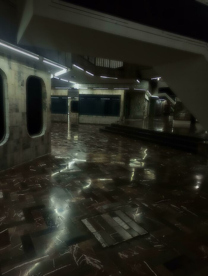 Dimly lit hall with futuristic lighting and reflective floors, resembling a videogame environment.