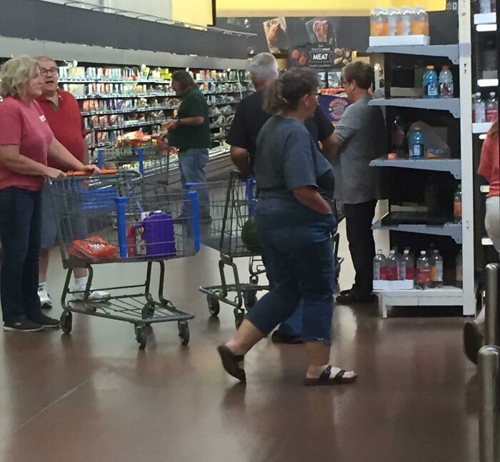 People blocking an aisle in a grocery store with shopping carts, appearing inconsiderate to others trying to pass.