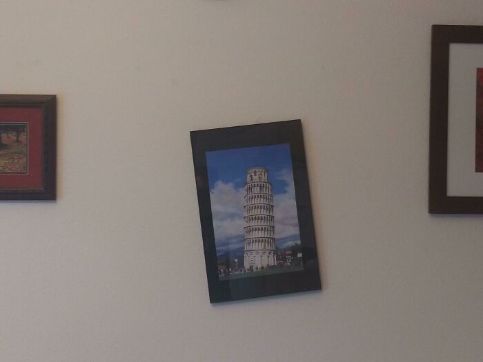 Crooked framed photo of Leaning Tower of Pisa on wall, showcasing lazy-infuriating-people tendencies.