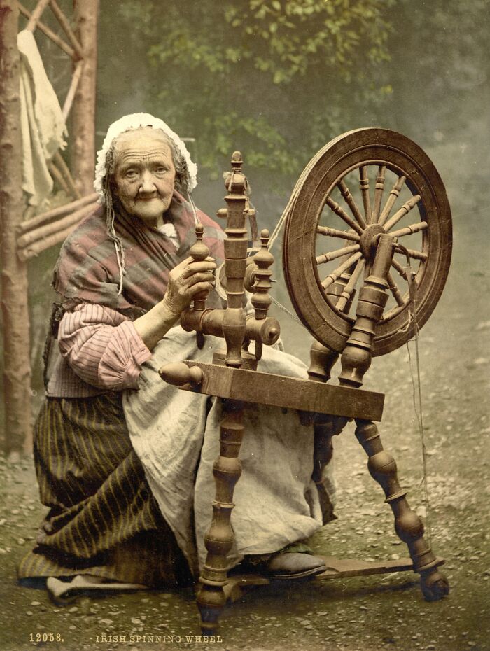 Elderly woman using an Irish spinning wheel, showcasing oldest color photography techniques from 100 years ago.