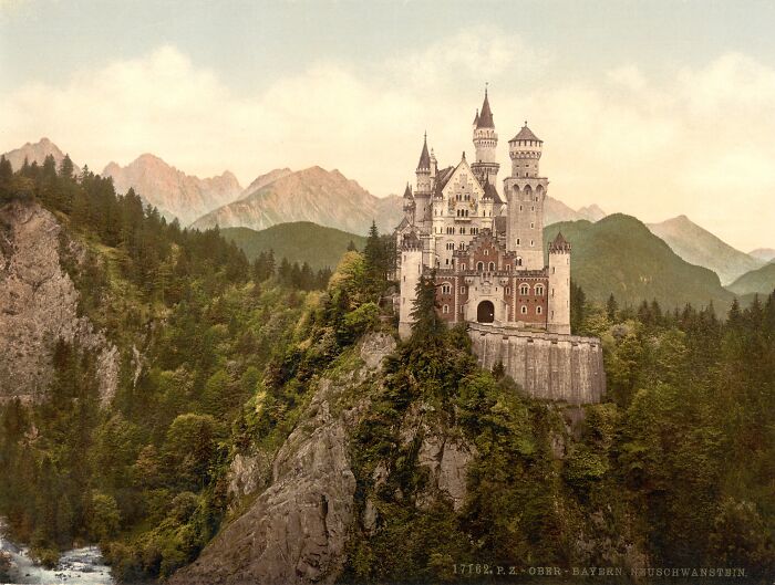 Neuschwanstein Castle in a vintage color photo, surrounded by mountains and forest, showcasing early 20th-century scenery.