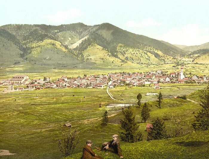 Historic color photo of Oberammergau village and surrounding hills, depicting life 100 years ago.