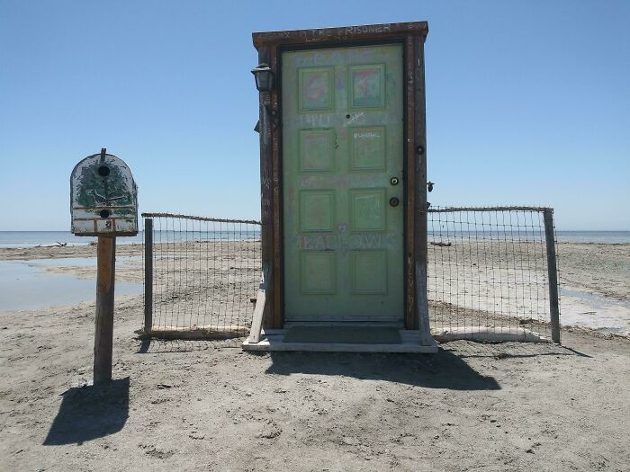 A green door and mailbox stand alone on a sandy beach, resembling a scene from a video game.