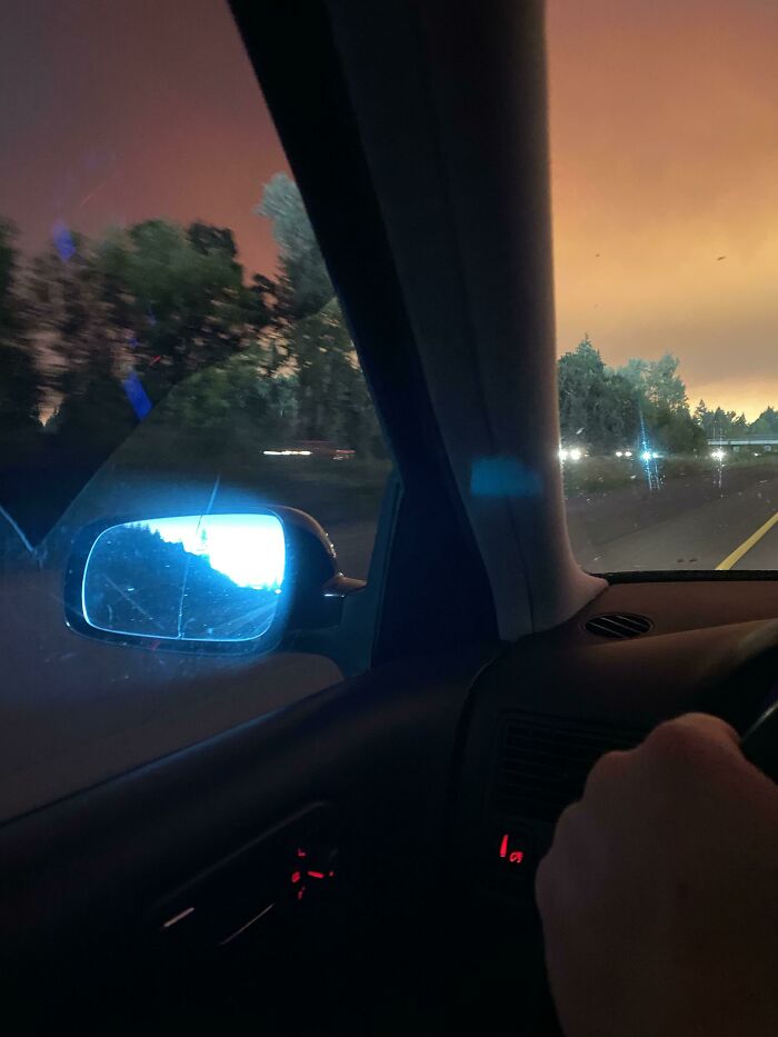 Driving scene with a sunset sky, resembling videogame graphics, reflecting in the car mirror.