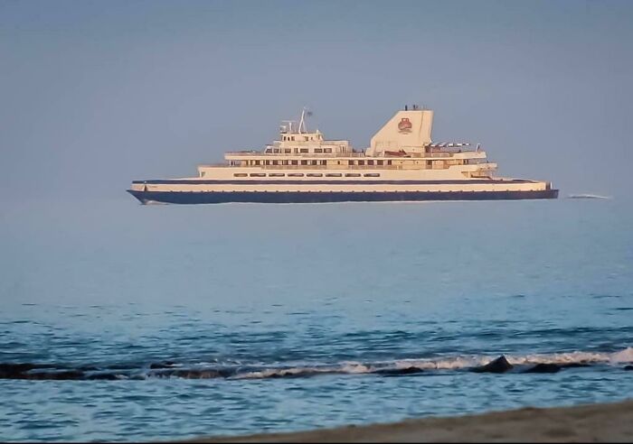 Large ferry appearing suspended over calm sea, resembling bad renders in real-life photos against a clear sky backdrop.