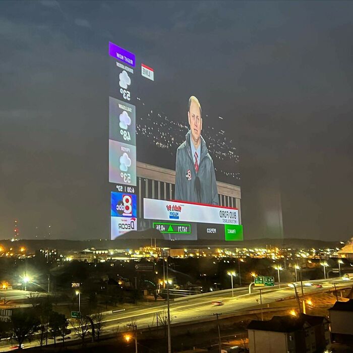 A weather broadcast projected in the sky over a city, resembling a scene from a video game.