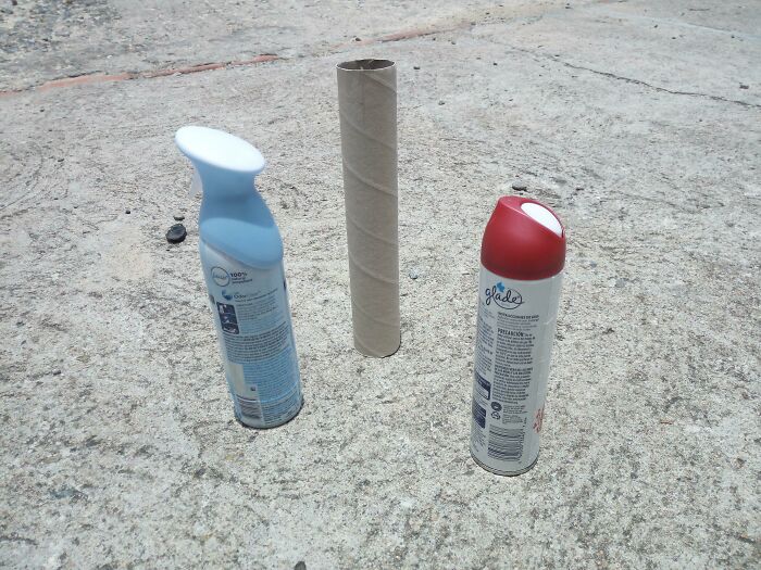 Three spray cans on concrete, resembling bad renders, with a cardboard tube in the center.