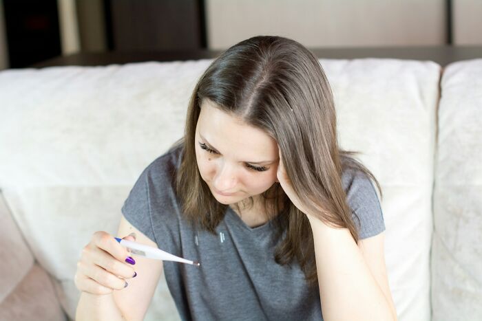 Woman looking at thermometer, appearing concerned about illness.