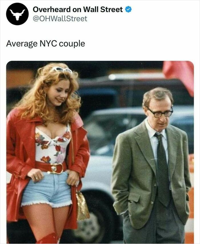 Man in suit and woman in red jacket walking on street, humorously captioned about NYC by Overheard on Wall Street.