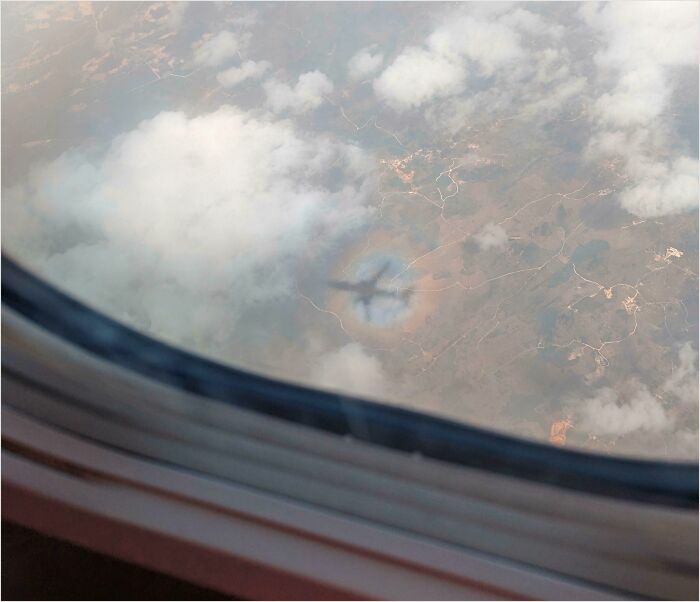 View from airplane window showing a perfect fit of the plane's shadow on clouds below.