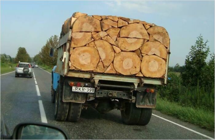 Truck loaded with logs showing a satisfying perfect fit, driving down a rural road.