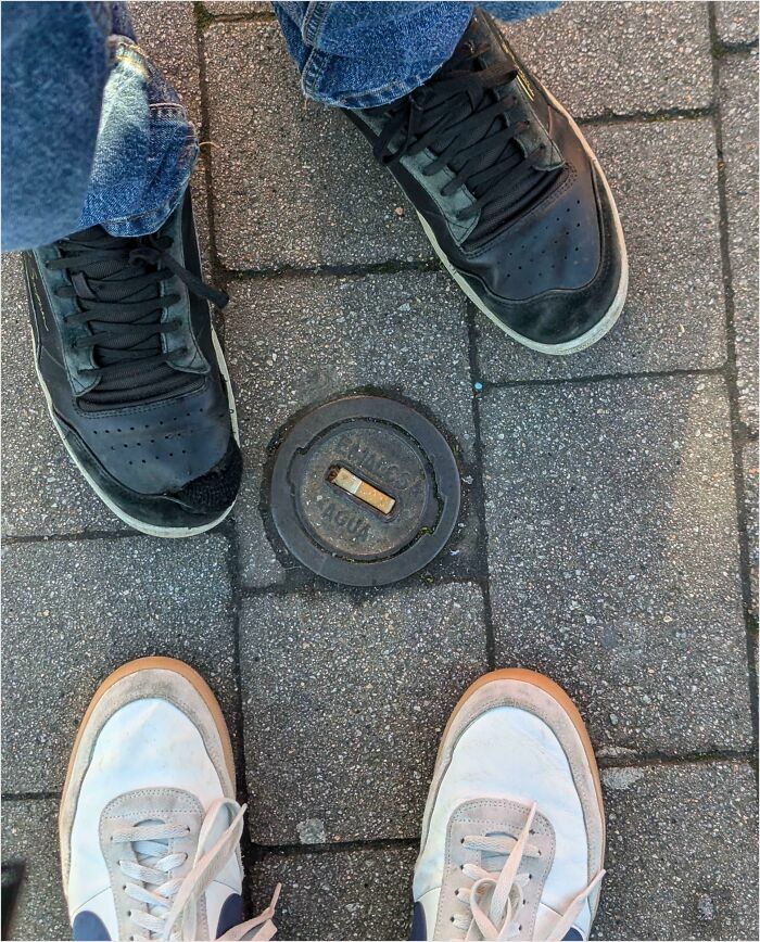 People wearing sneakers standing around a perfectly fitted utility cover on a sidewalk.