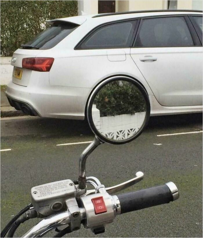 Motorbike mirror reflecting perfectly aligned car and wall, creating a satisfying perfect fit.