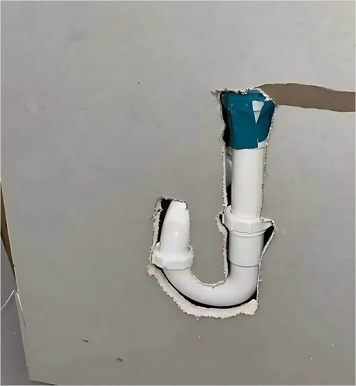 Uneven wall cutout exposing a misaligned pipe, representing a construction fail.