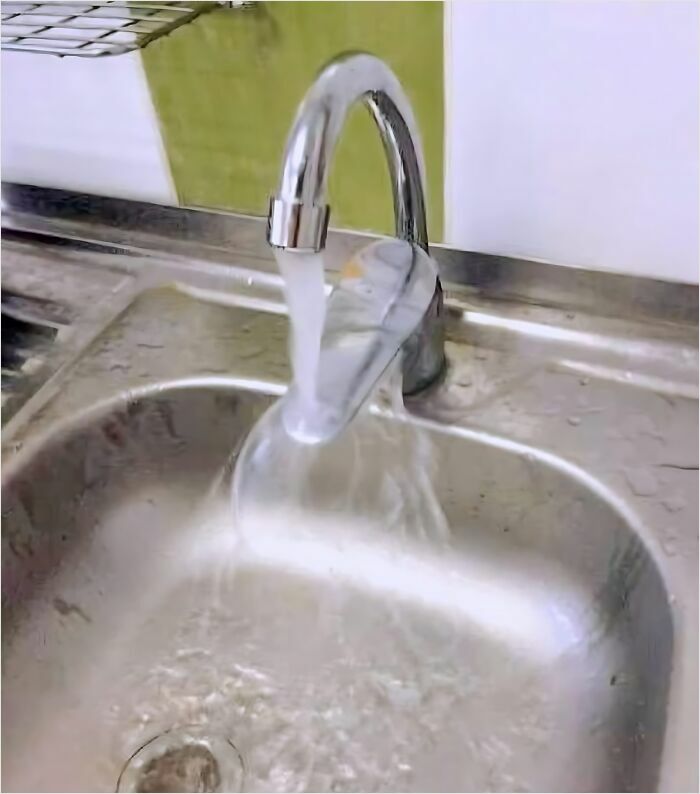 A faucet misaligned with a sink, showcasing a construction fail with water splashing outside the basin.