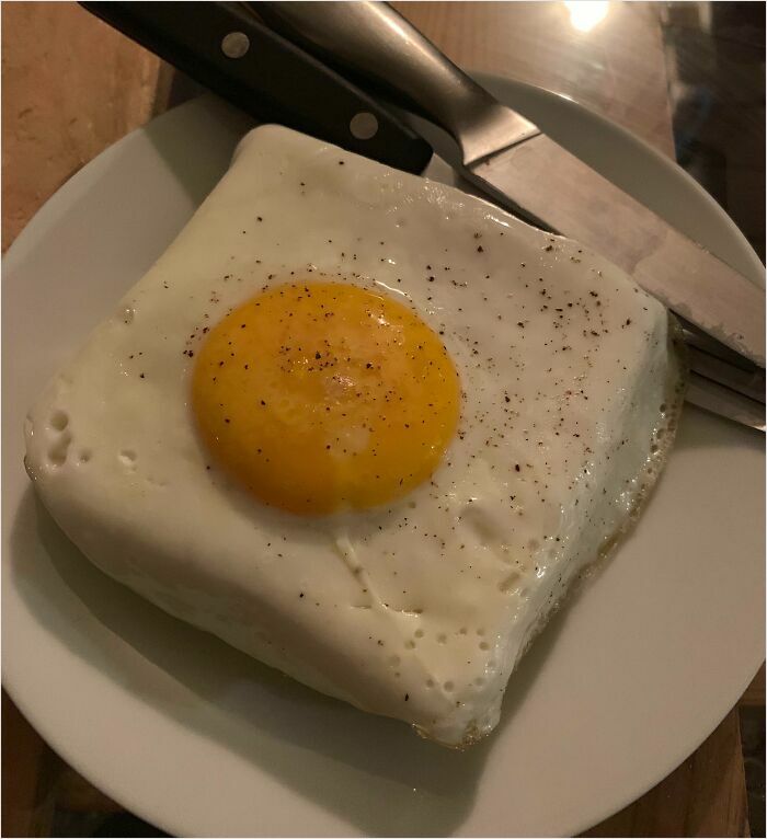 Square-shaped fried egg on a plate, showcasing a perfect fit with a knife beside it.