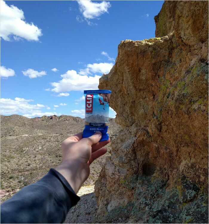 Hand holding a snack bar against a rock formation, achieving a satisfying perfect fit with the landscape background.