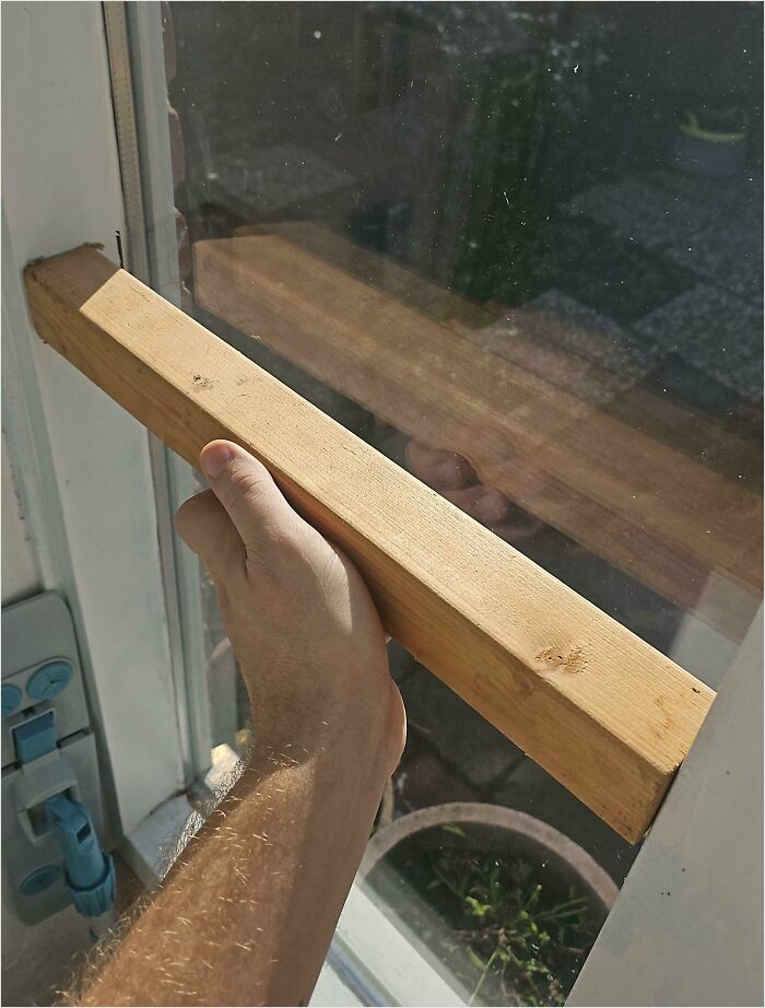 Hand holding a wooden plank fitting perfectly into a window frame, illustrating a satisfying perfect fit.